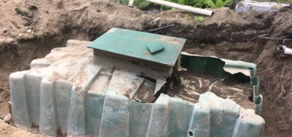 3 tips to help extend the life of your septic 2 3 Tips To Extend The Life Of Your Septic Tank - A rusty, green septic tank is partially unearthed in a dirt hole, revealing damaged and broken sections. The surrounding area is scattered with dirt and debris. Some exposed pipes are visible in the background, running along the edge of the hole. Shrubs and greenery are seen further back. Greenleaf Excavation Muskoka